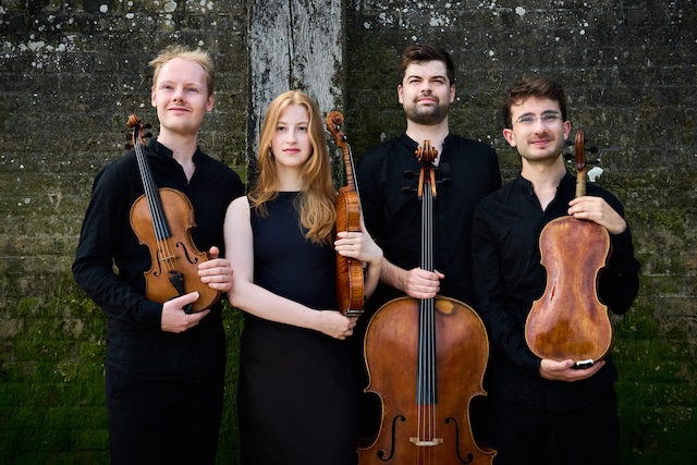 Four performers with their instruments in a woodland setting.